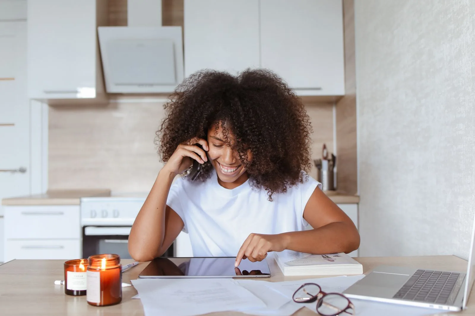A woman discussing information by phone while reviewing a tablet and notes at home