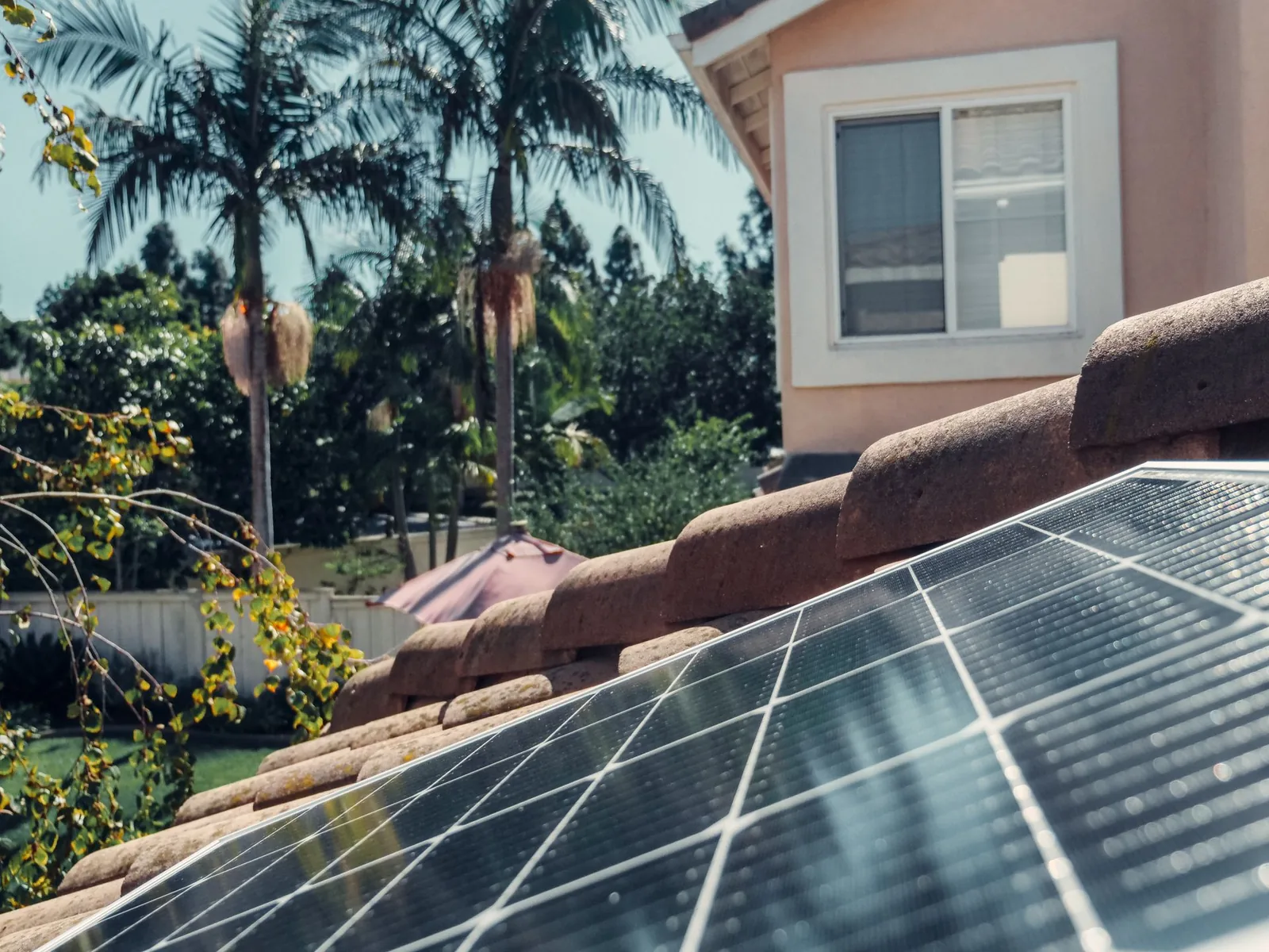 Solar panels on a tiled residential roof beside a stucco home and palms in California