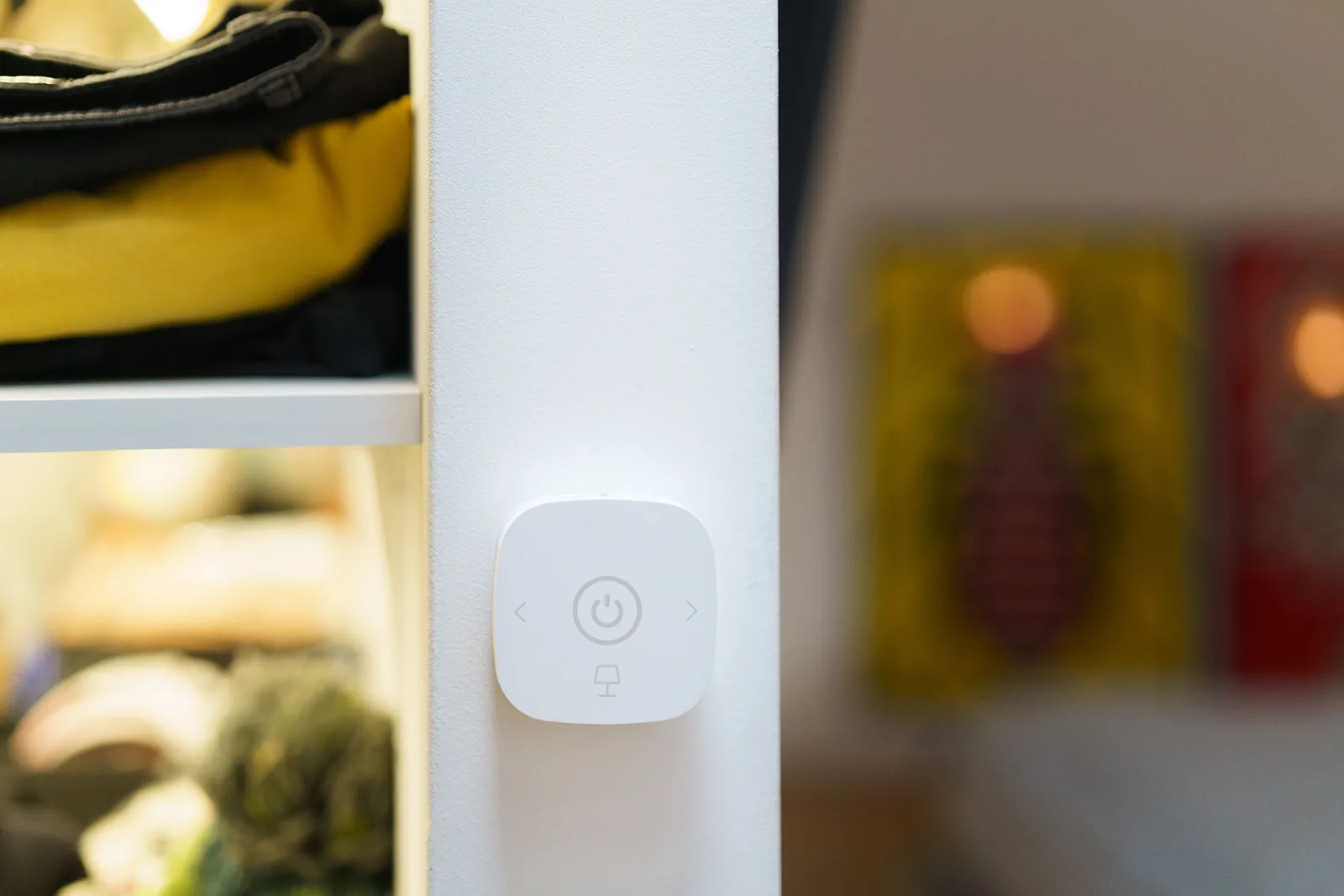 A wall-mounted wireless lighting control beside illuminated shelving